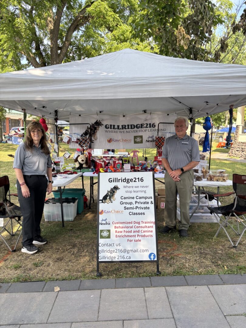 Two people stand beside a booth promoting a wellness center at an outdoor event.